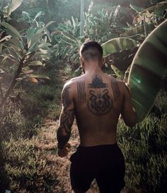 a man walking through the woods with tattoos on his back