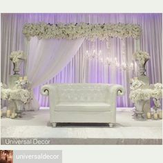 a white couch sitting in front of a purple and white drape covered stage with flowers on it