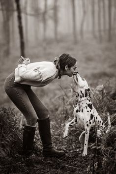 a woman kissing a dalmatian dog in the woods