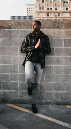 a man leaning against a wall with his hands clasped