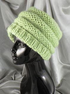 a mannequin head wearing a green knitted hat on top of a white cloth