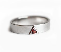 a white gold ring with a red stone in the middle and a triangle on top