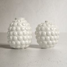 two white vases sitting next to each other on a gray surface with no one around them