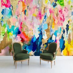 two green chairs sitting in front of a colorful wall