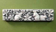 a decorative piece with rabbits and flowers in the center on a green wall behind it