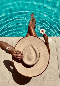 a woman laying on the ground next to a swimming pool wearing a hat and bracelets