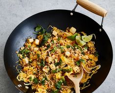 a pan filled with rice and vegetables on top of a table next to a wooden spoon