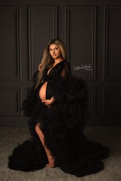 a pregnant woman in a black gown posing for the camera with her hands on her hips