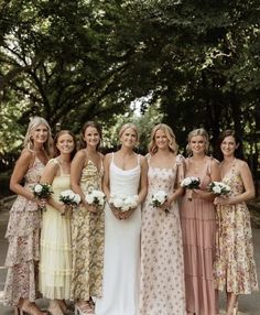 a group of women standing next to each other wearing dresses and holding bouquets in their hands