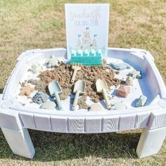 a sandbox with shovels and rocks in it on the grass, next to a sign