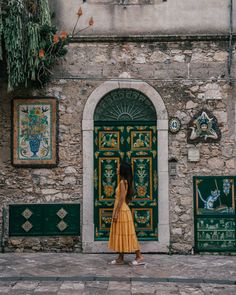 a woman standing in front of a building with green doors and paintings on the wall