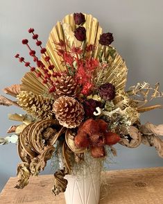 a white vase filled with lots of different types of flowers and leaves on top of a wooden table