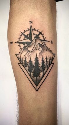 a man's leg with a compass tattoo on it and mountains in the background