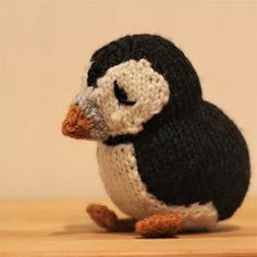 a small knitted penguin sitting on top of a wooden table next to a wall