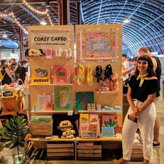 a woman standing in front of a booth at a craft fair with lots of cards on display