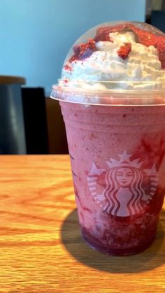 a starbucks drink with whipped cream and strawberries in it sitting on a wooden table