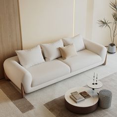 a living room with white couches and pillows on top of the sofa is next to a potted plant