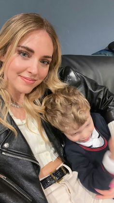 a woman sitting next to a little boy in a black leather jacket and white shirt