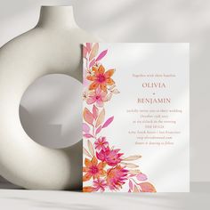 a white vase with a pink and orange flower on it next to a wedding card