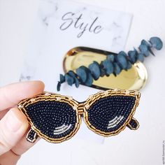 a pair of black and gold sunglasses with beaded details on the front, sitting next to a hair clip