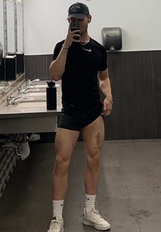 a man taking a selfie with his cell phone in a public restroom while wearing shorts and socks