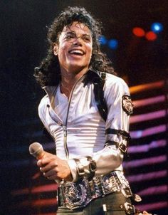 michael jackson singing into a microphone on stage with his hands in his pockets and one hand out to the side