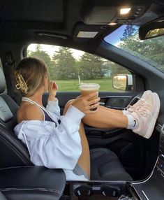 a woman sitting in the back seat of a car holding a drink