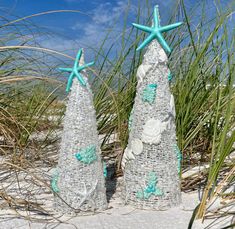 two plastic christmas trees sitting on top of a sandy beach covered in sand and sea grass