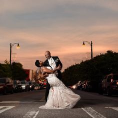 a bride and groom are standing in the middle of the street at sunset with their arms around each other