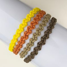 four crocheted bracelets are lined up on a white surface and one is yellow, the other is brown