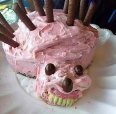 a pink frosted cake with chocolate sticks sticking out of it's face on a white plate