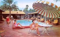 several women sitting around a swimming pool with an umbrella over the pool and chairs in front of it