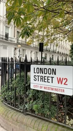 a street sign on a fence in front of a building with trees and bushes behind it