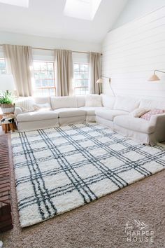 a living room with white couches and rugs on the floor in front of windows