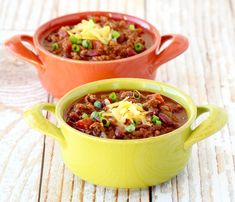 two bowls filled with chili and cheese on top of a wooden table next to each other