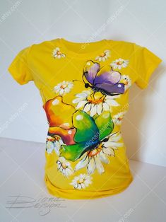 a yellow t - shirt with butterflies and daisies painted on it's chest