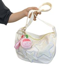 a hand holding a white purse with a pink pig on it's side and a star shaped keychain hanging from the strap