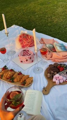 a table topped with cakes and desserts on top of a lush green field next to a forest