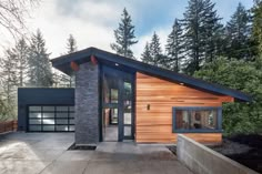 a modern house in the woods with wood siding and stone accents on the front door