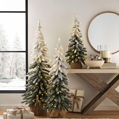 two christmas trees are decorated with white lights and gold garlands in front of a window