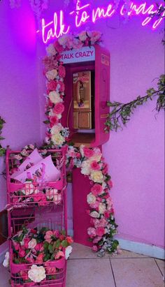 a pink vending machine with flowers on the wall next to it and a neon sign that says talk to me crazy