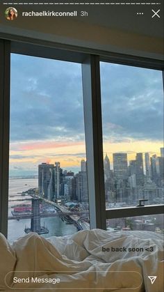 a bed sitting in front of a window next to a large cityscape on the side of a tall building