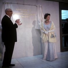 an older man and woman standing in front of a wall that has writing on it