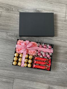 a gift box filled with chocolates, candy and roses on top of a wooden floor