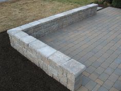 a stone bench sitting on top of a brick patio next to a grass covered field