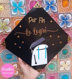 a hand holding a graduation cap with the words por fin de logre written on it