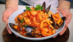 a person holding a plate of pasta with shrimp and mussels on it,