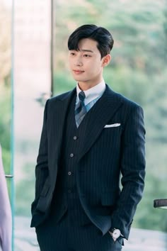 a young man in a suit and tie standing next to a glass wall looking at the camera