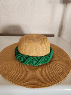 a straw hat with green yarn around the brim on a white countertop next to a wall