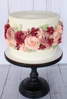 a white cake with pink and red flowers on it sitting on top of a wooden table